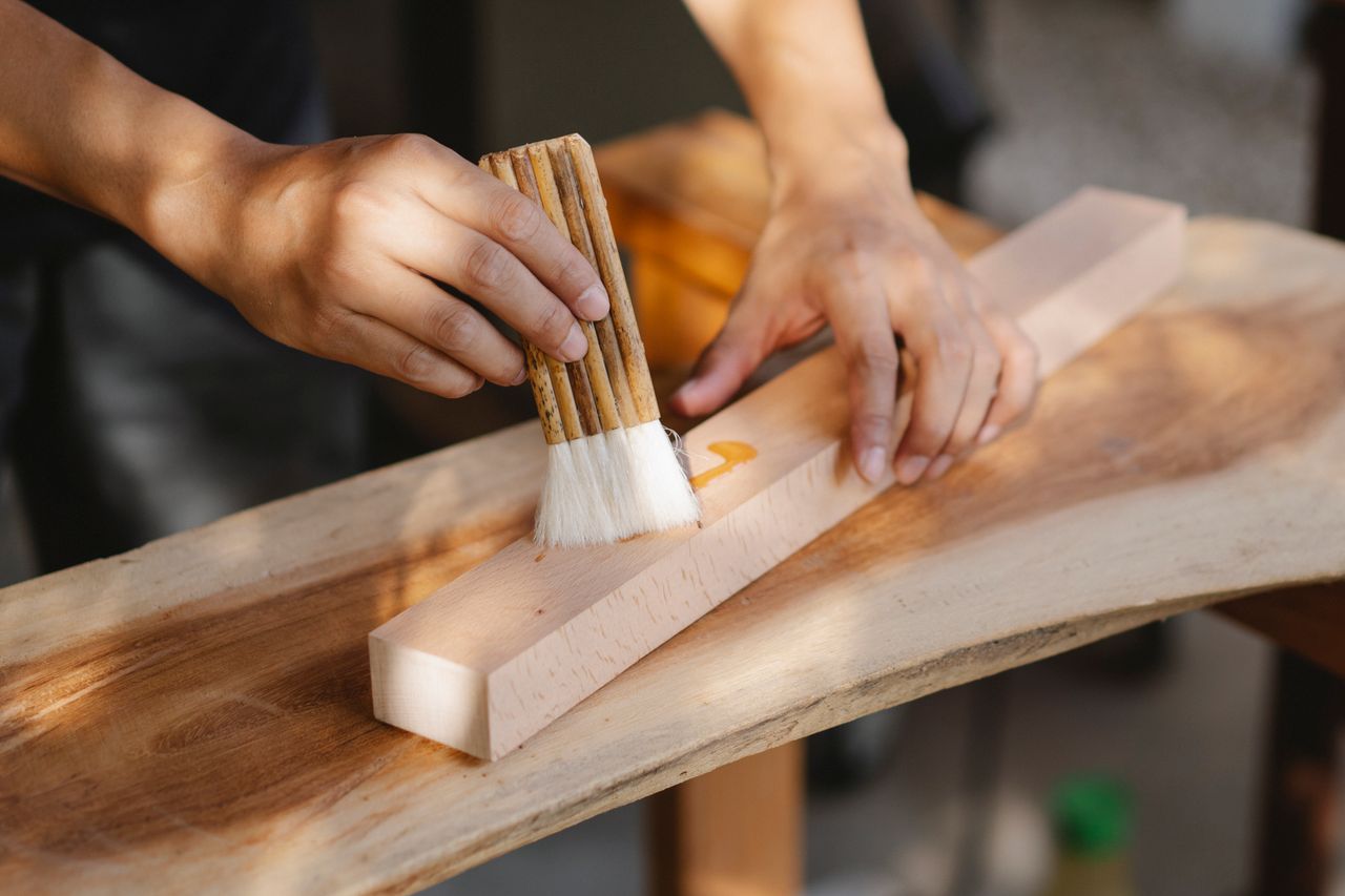 High angle of crop anonymous male artisan oiling wooden plank with brush while working in workshop