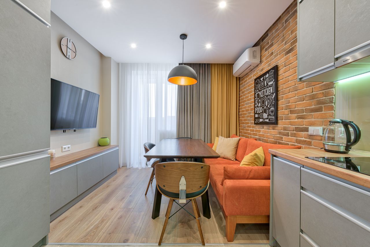 Stylish apartment interior with a brick wall, orange sofa, and wooden furniture.